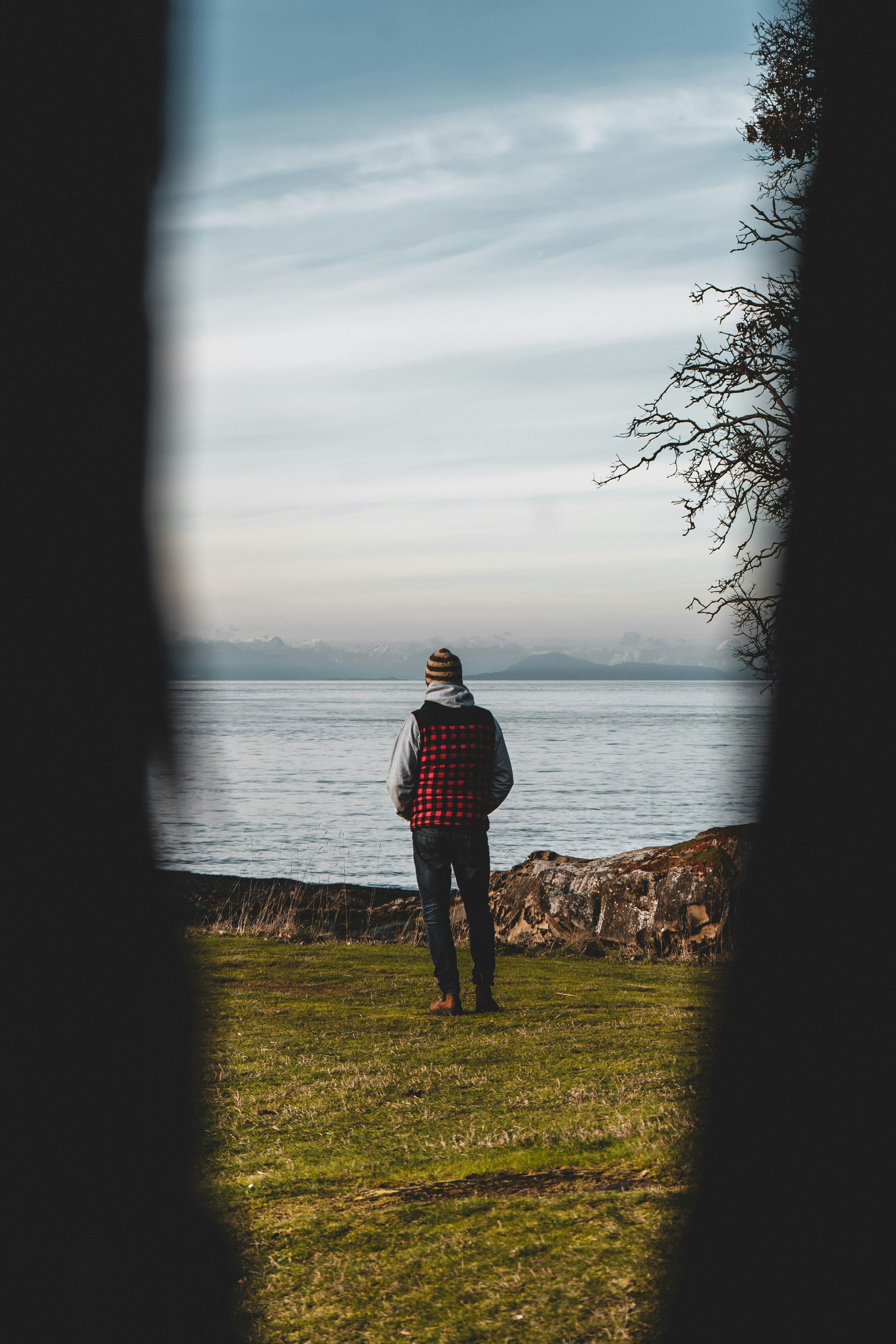 man in black and white plaid dress shirt standing on rock near body of water during